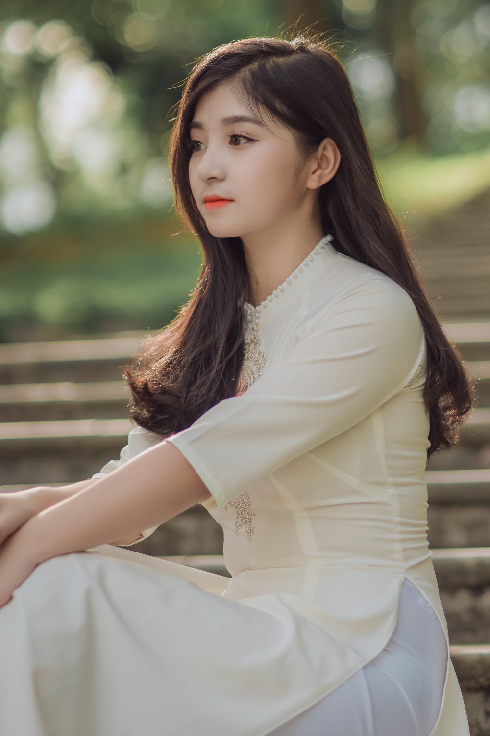 Linh, seated on outdoor steps in a pale dress